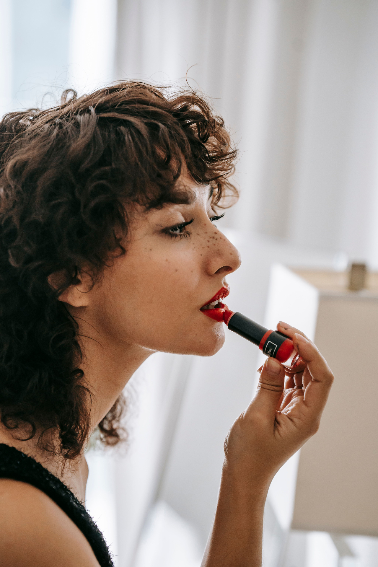 Ragazza dai capelli ricci si mette il rossetto rosso davanti allo specchio, in una stanza luminosa